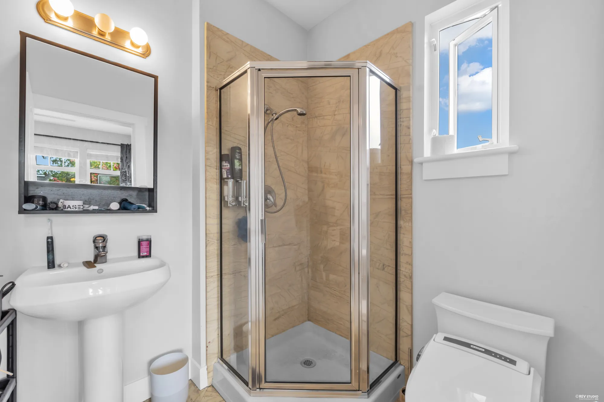 A bathroom with a corner shower, a pedestal basin and a window