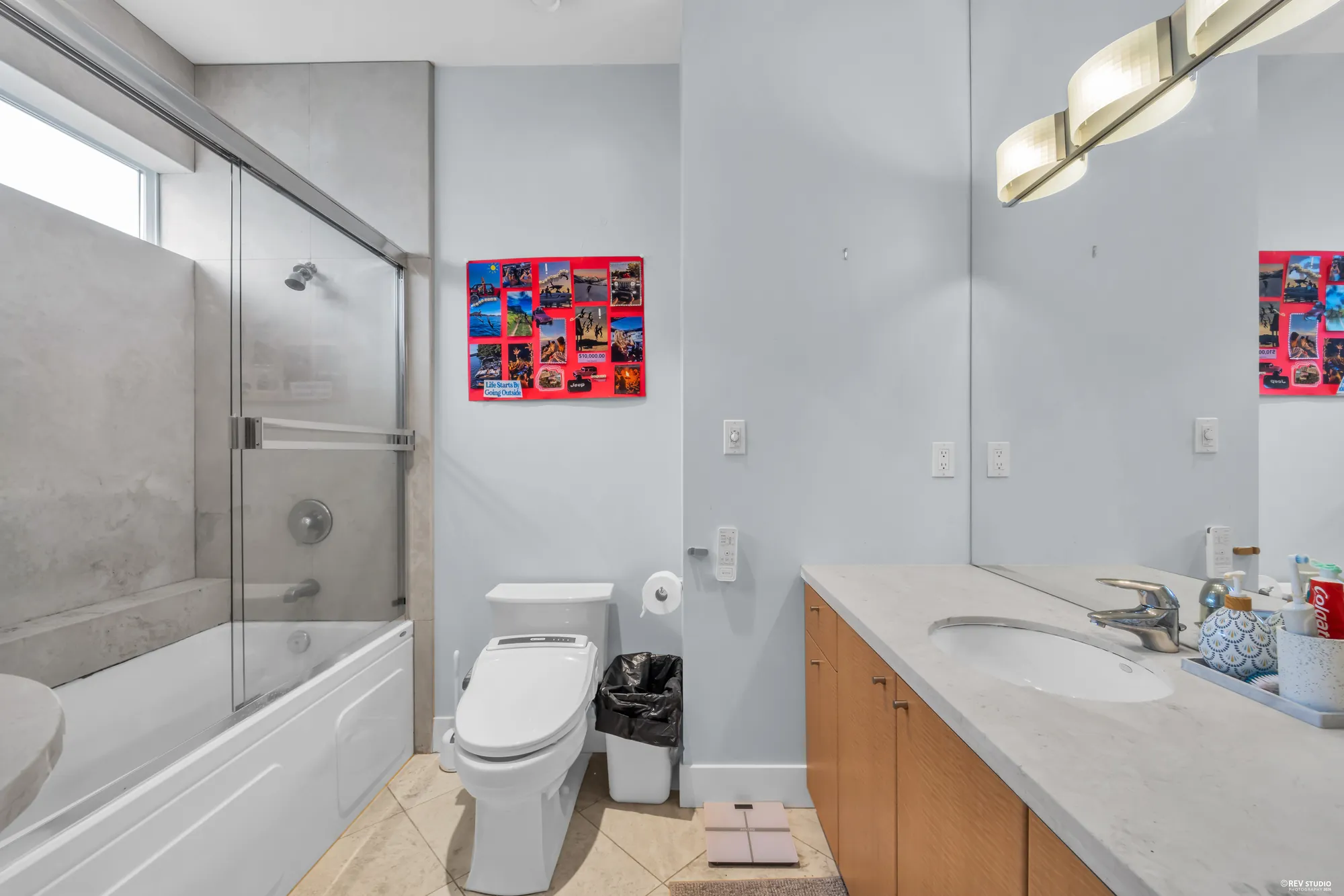 The hall bathroom: a tub and shower behind glass, a vanity under a strip light