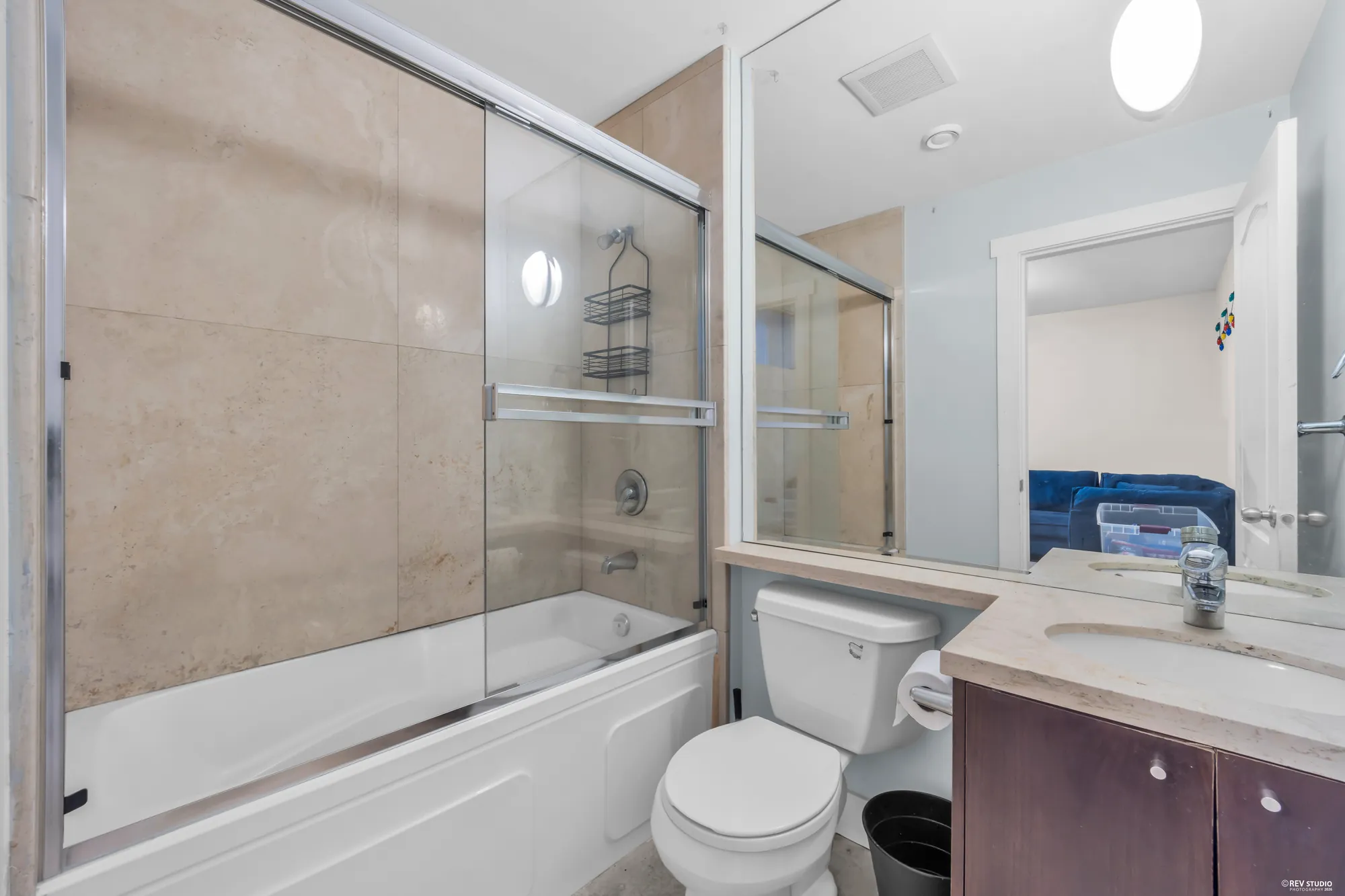 A lower bathroom with a tub and shower behind a glass door, stone-look tile