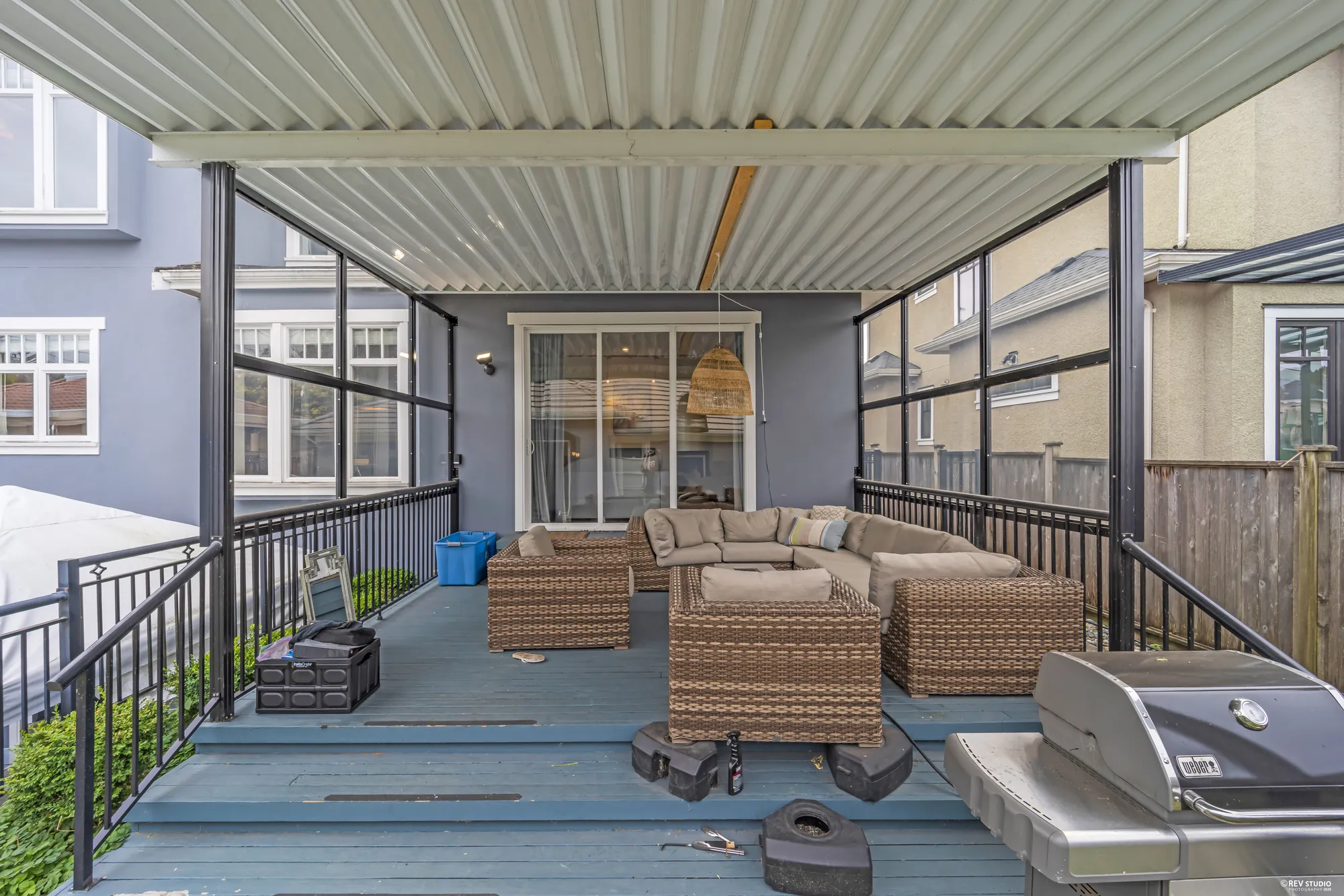 Under the deck roof: wicker sofas around a fire table, the barbecue, the garden beyond the rail