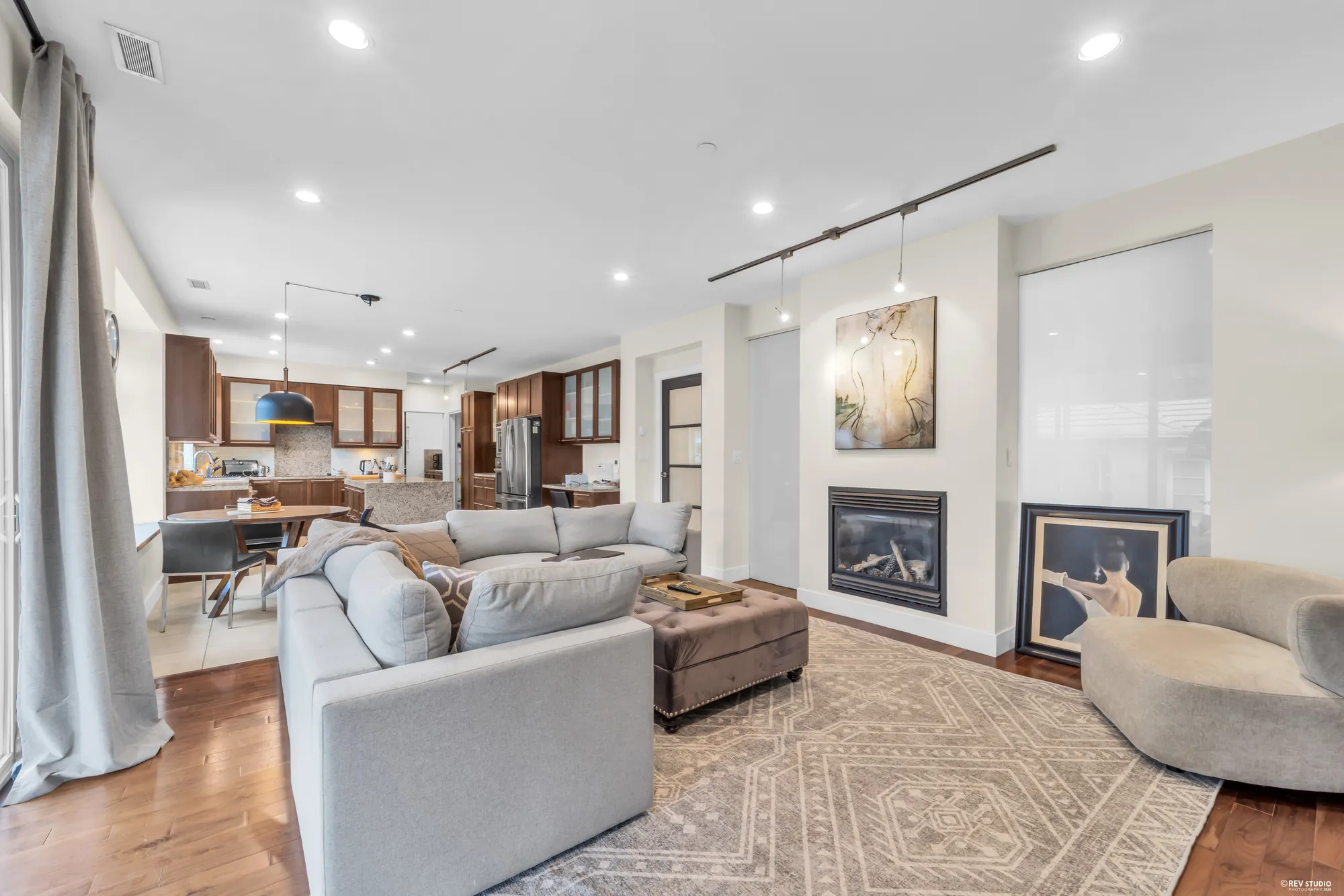 The family room: a fireplace between windows, a sectional on a rug, the kitchen open beyond