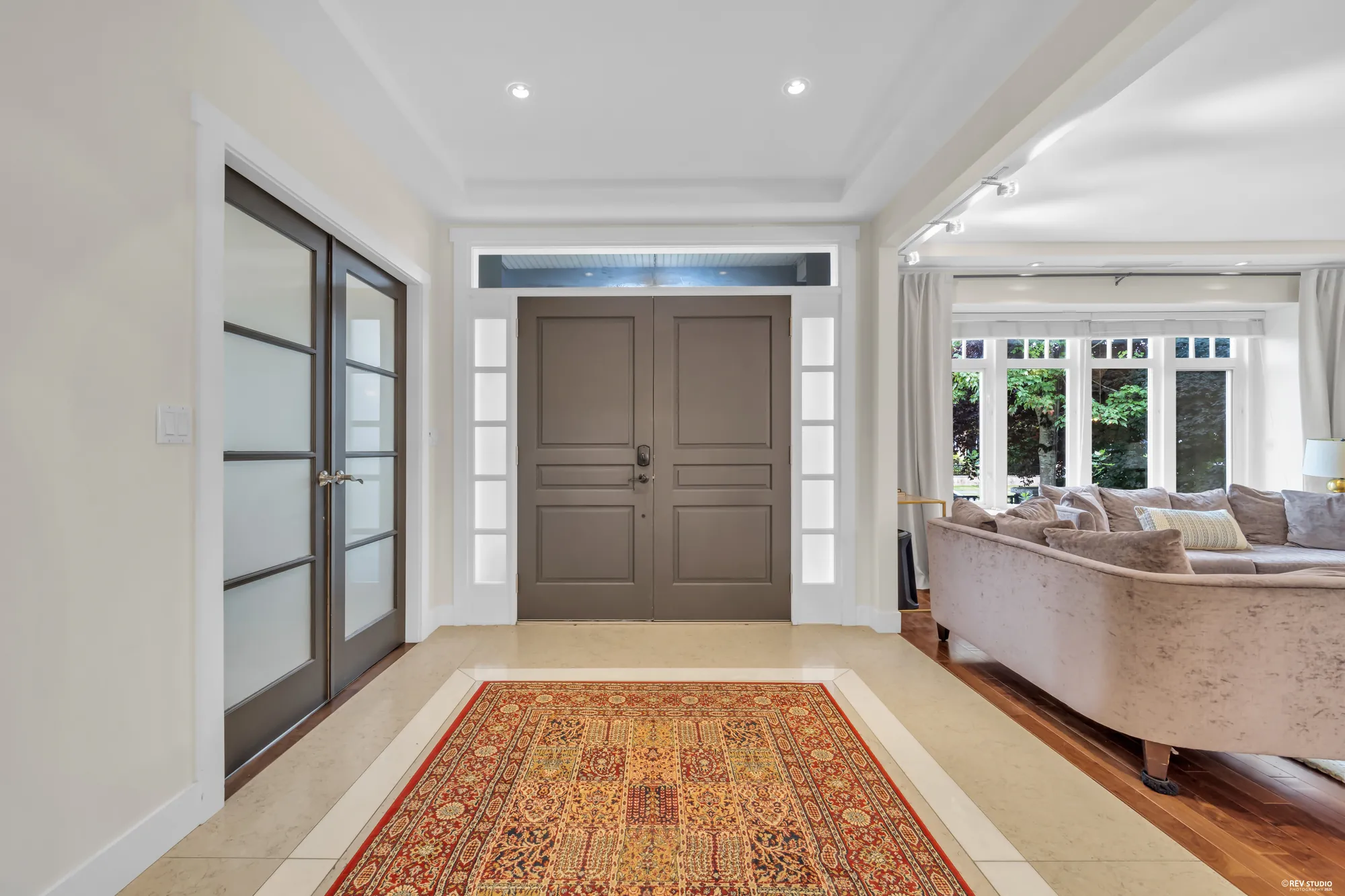 The foyer: the double front door with glazed panels, a black-framed glass door to the office at left, a rug on the tile