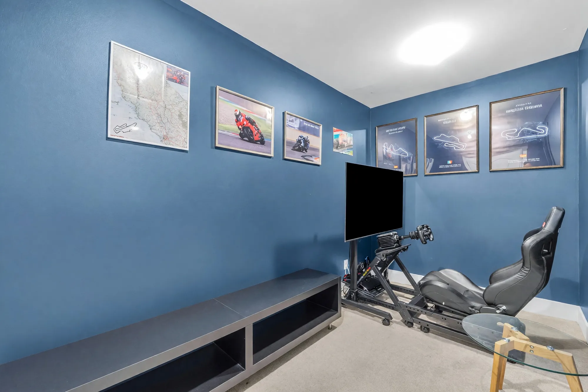 The game room: navy walls with framed motorcycle prints, a racing simulator seat, a screen on a stand