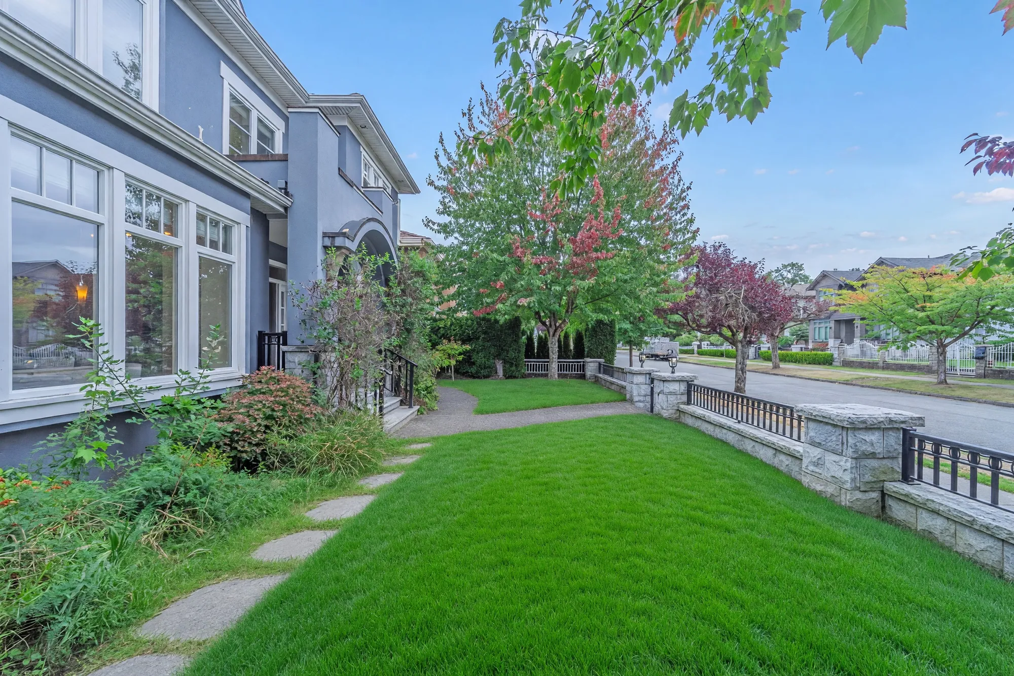 The garden between the side of the house and the front wall, a paved path, a maple and the street beyond