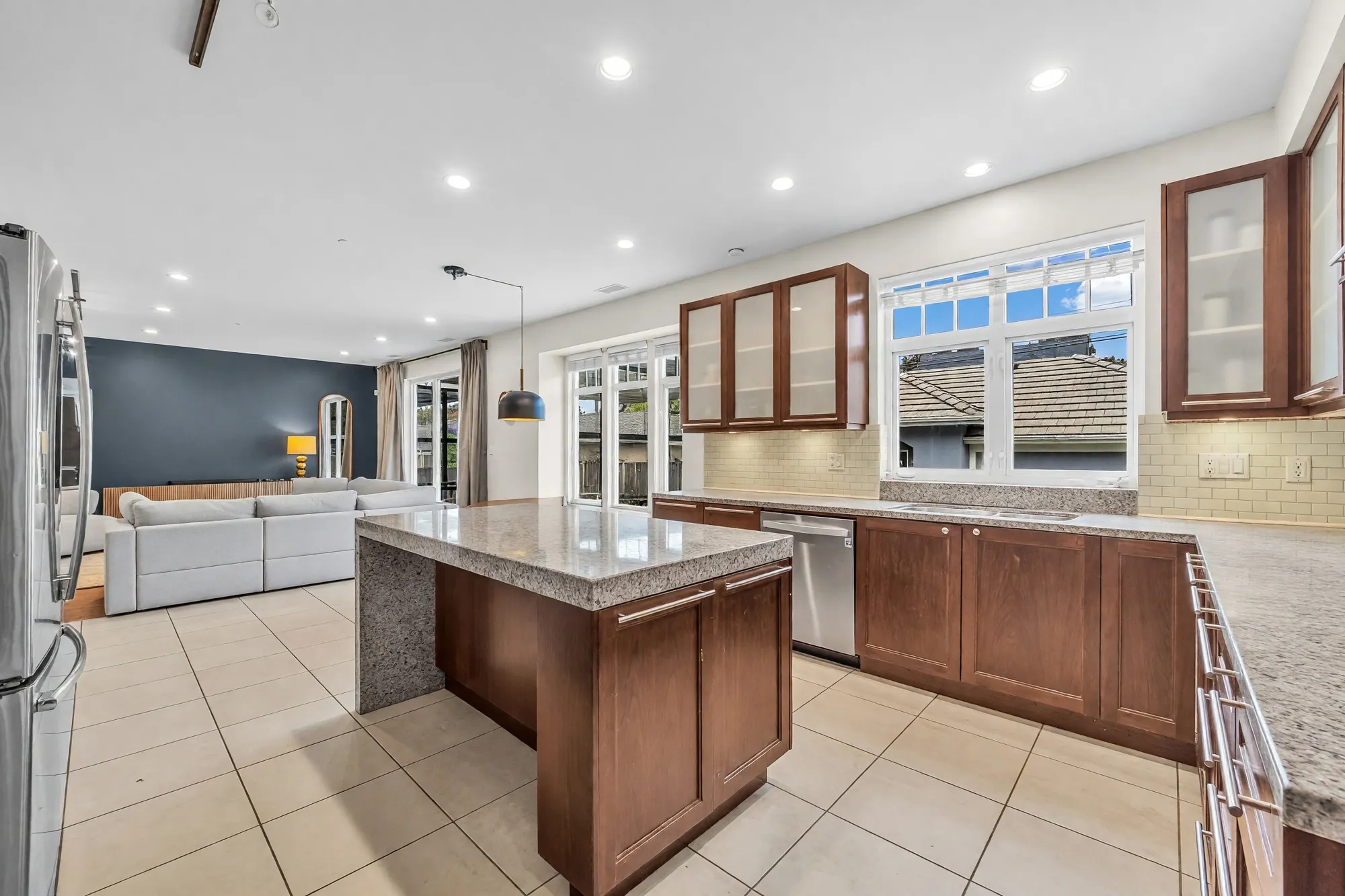 The kitchen: a granite island with cherry cabinetry, glass-fronted upper cabinets, windows over the counter, the family room beyond