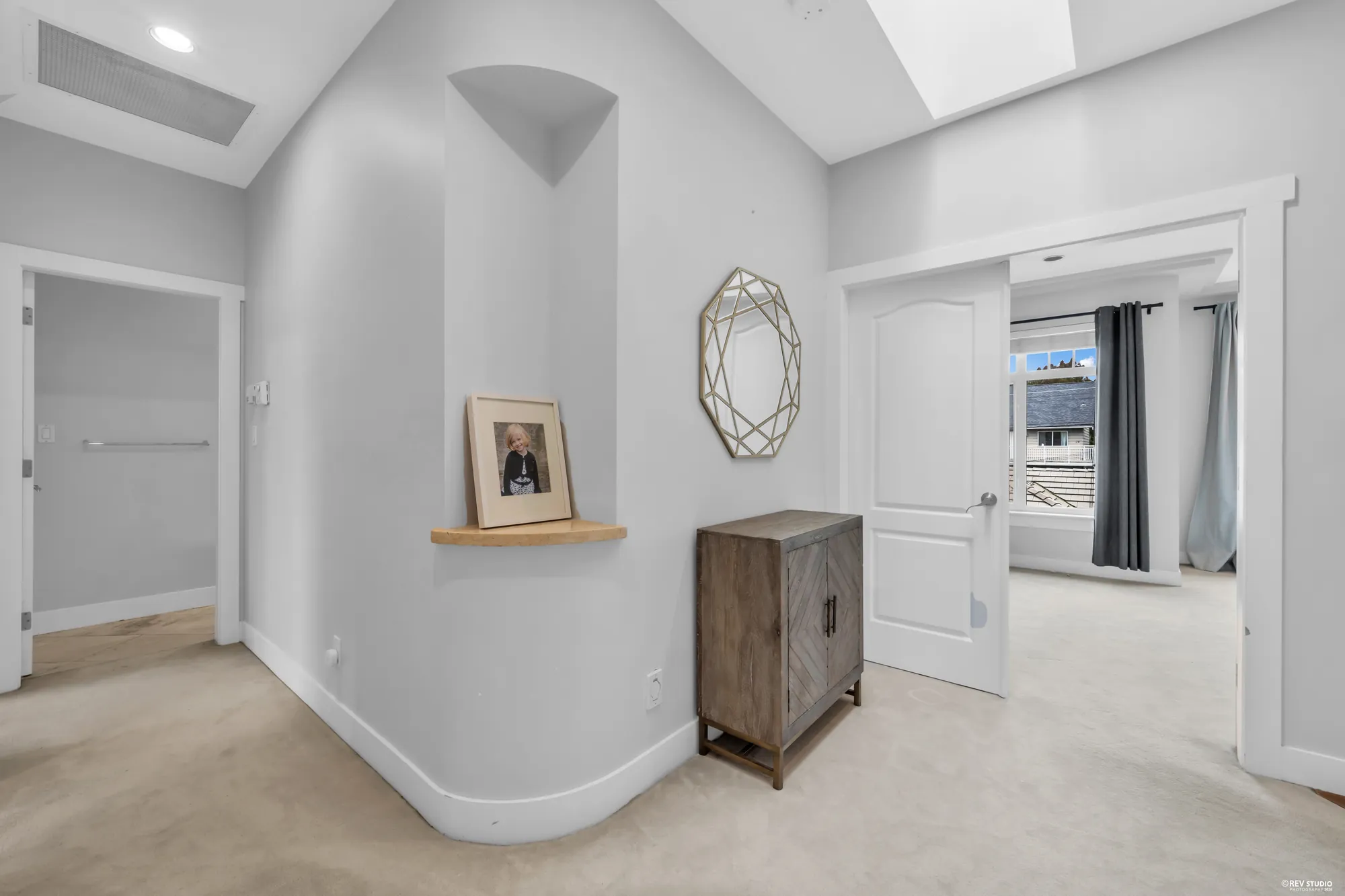 The upper hall under a vaulted ceiling with a skylight, doors to the bedrooms