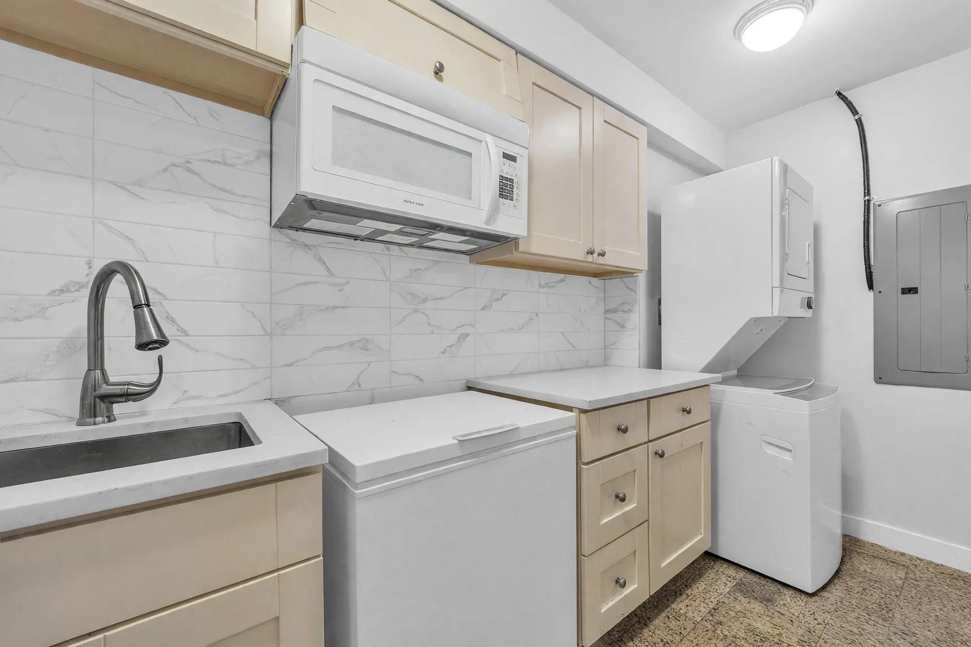 The lower laundry: a sink and cabinets under a microwave, a stacked washer and dryer, the electrical panel