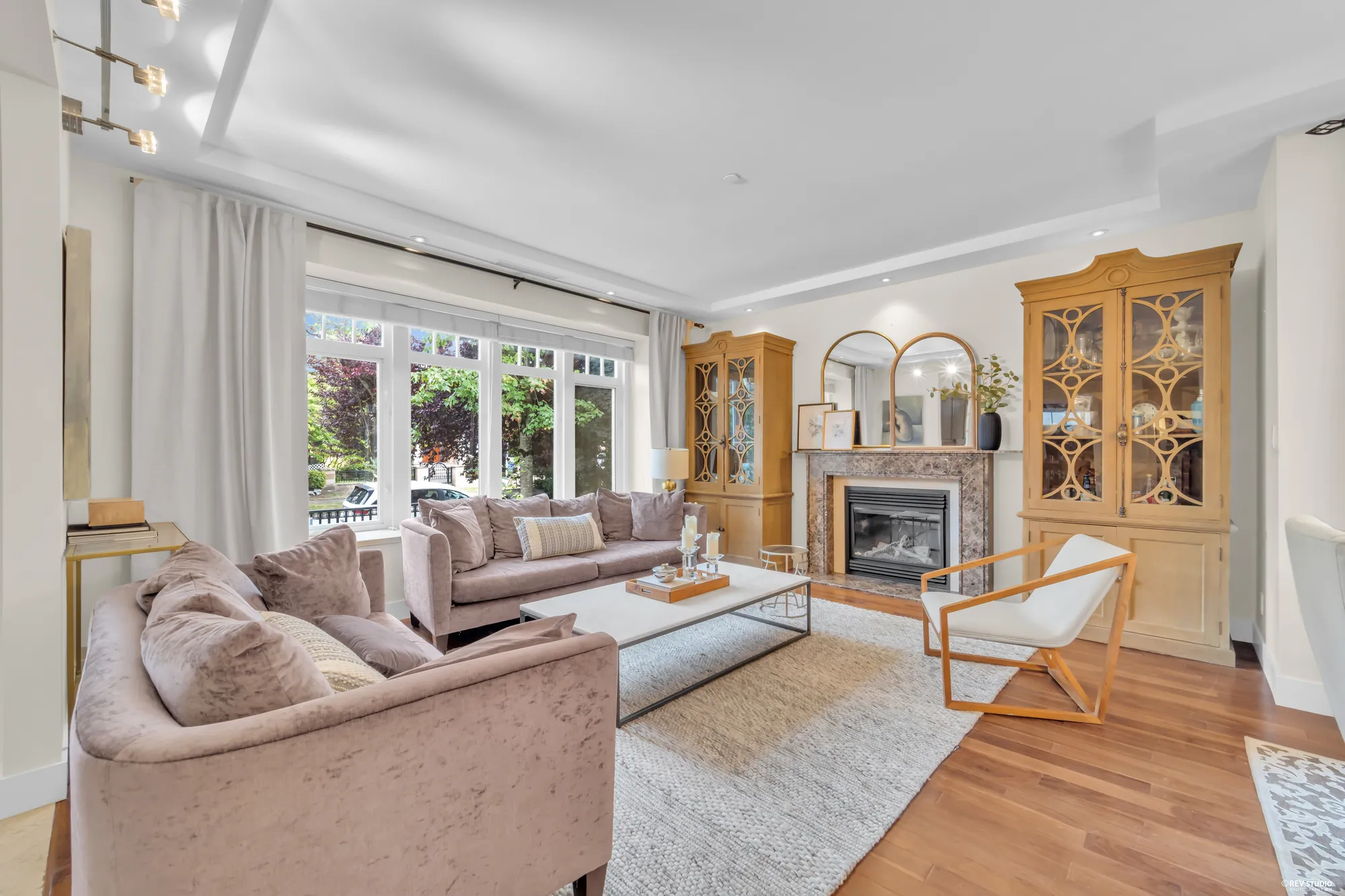The living room: a fireplace in a stone surround between two glazed cabinets, sofas on a rug, doors and windows to the front garden