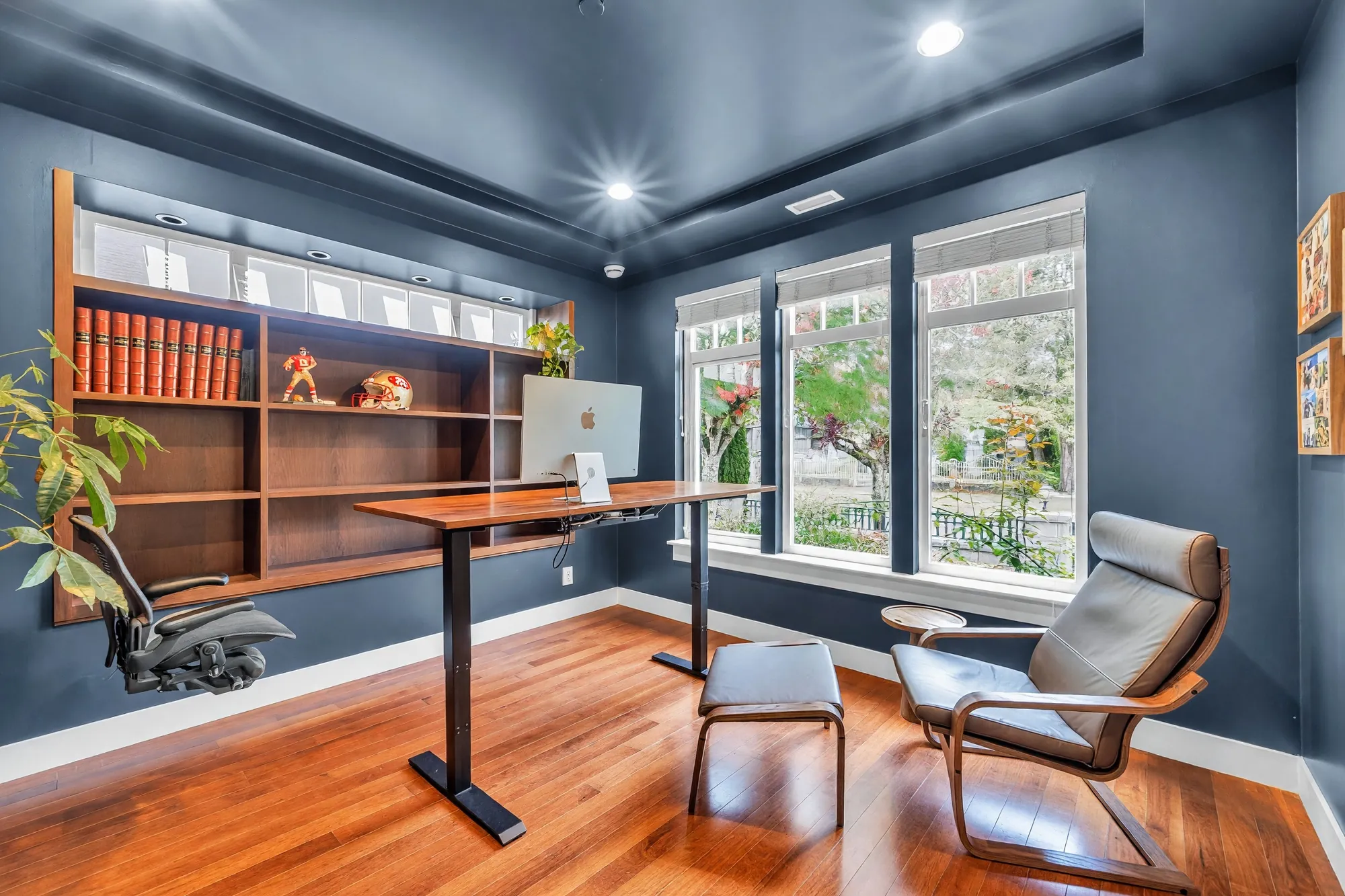 The office: navy walls, a wall of built-in shelves with books, a standing desk, two chairs, windows onto the street