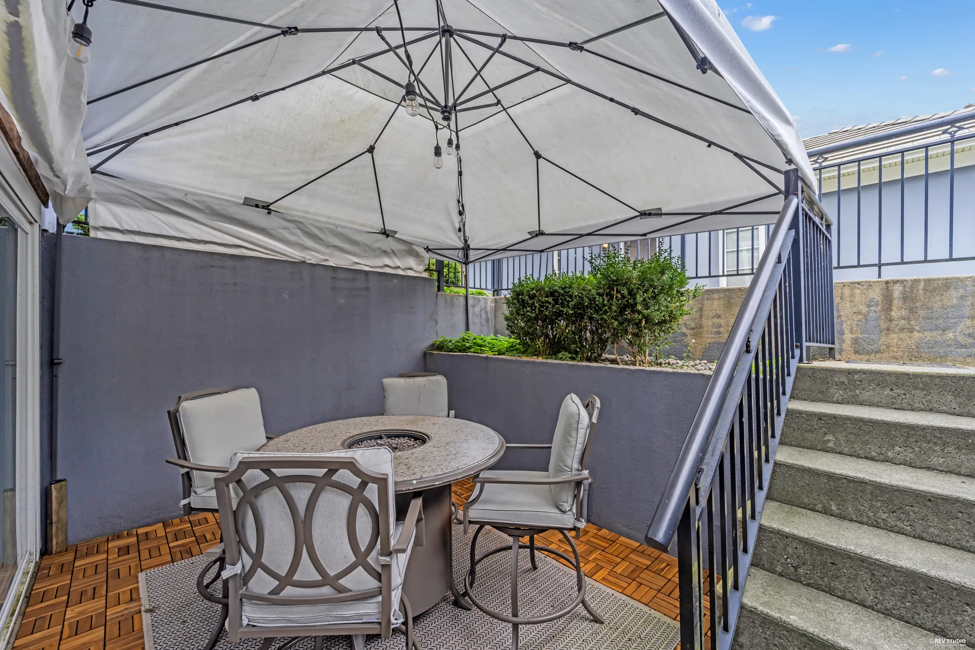 The lower patio under a canopy: a round fire table with chairs, the stair up to the deck