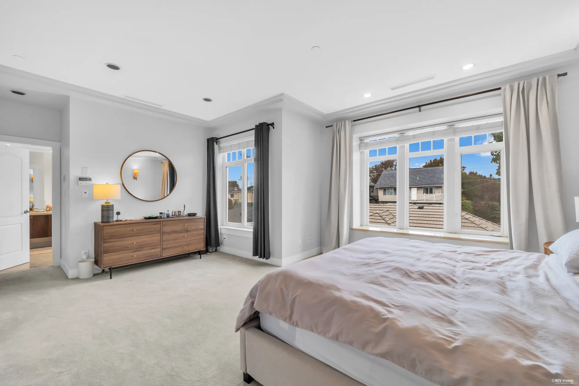 The primary bedroom toward the dresser with its round mirror and the two windows