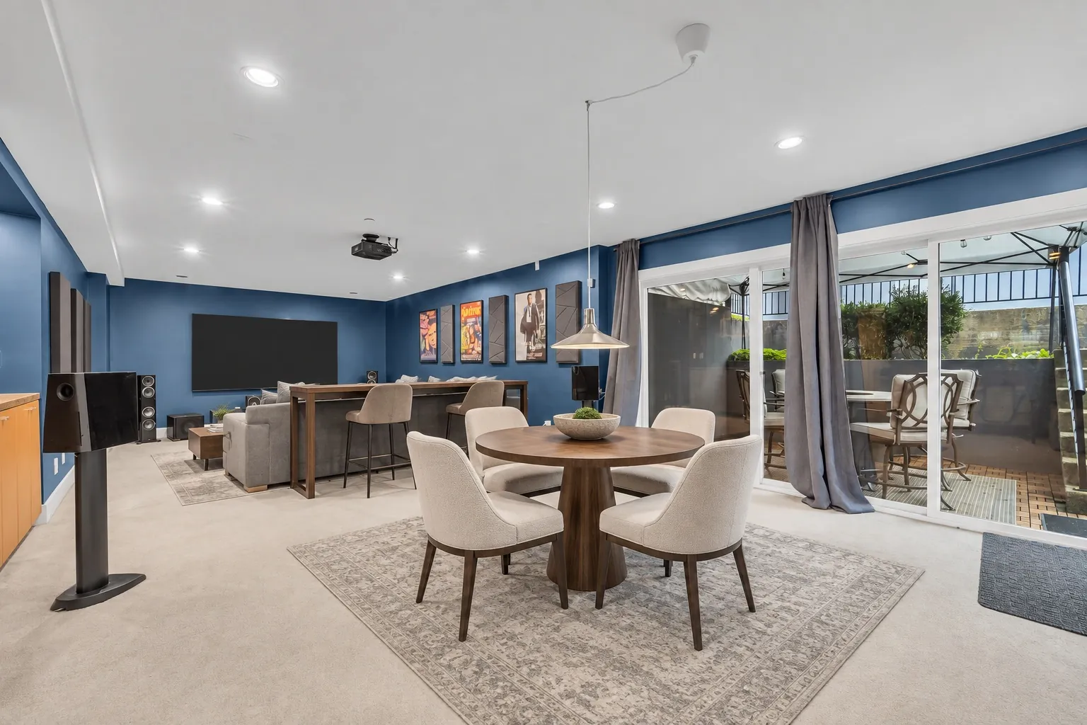 The recreation room, navy walls, virtually staged with a round table and chairs on a rug, a sofa and a bar with stools, the doors to the patio at right