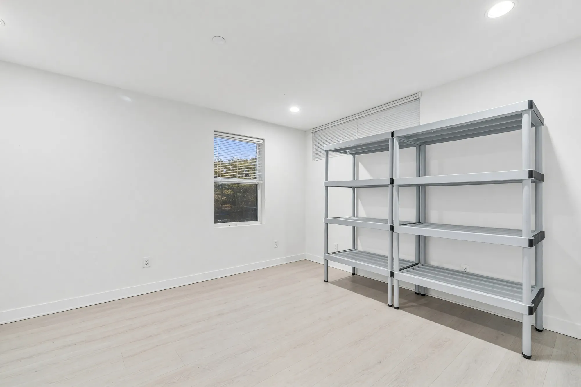 A finished storeroom with a metal shelving unit, a small window and a wood-look floor