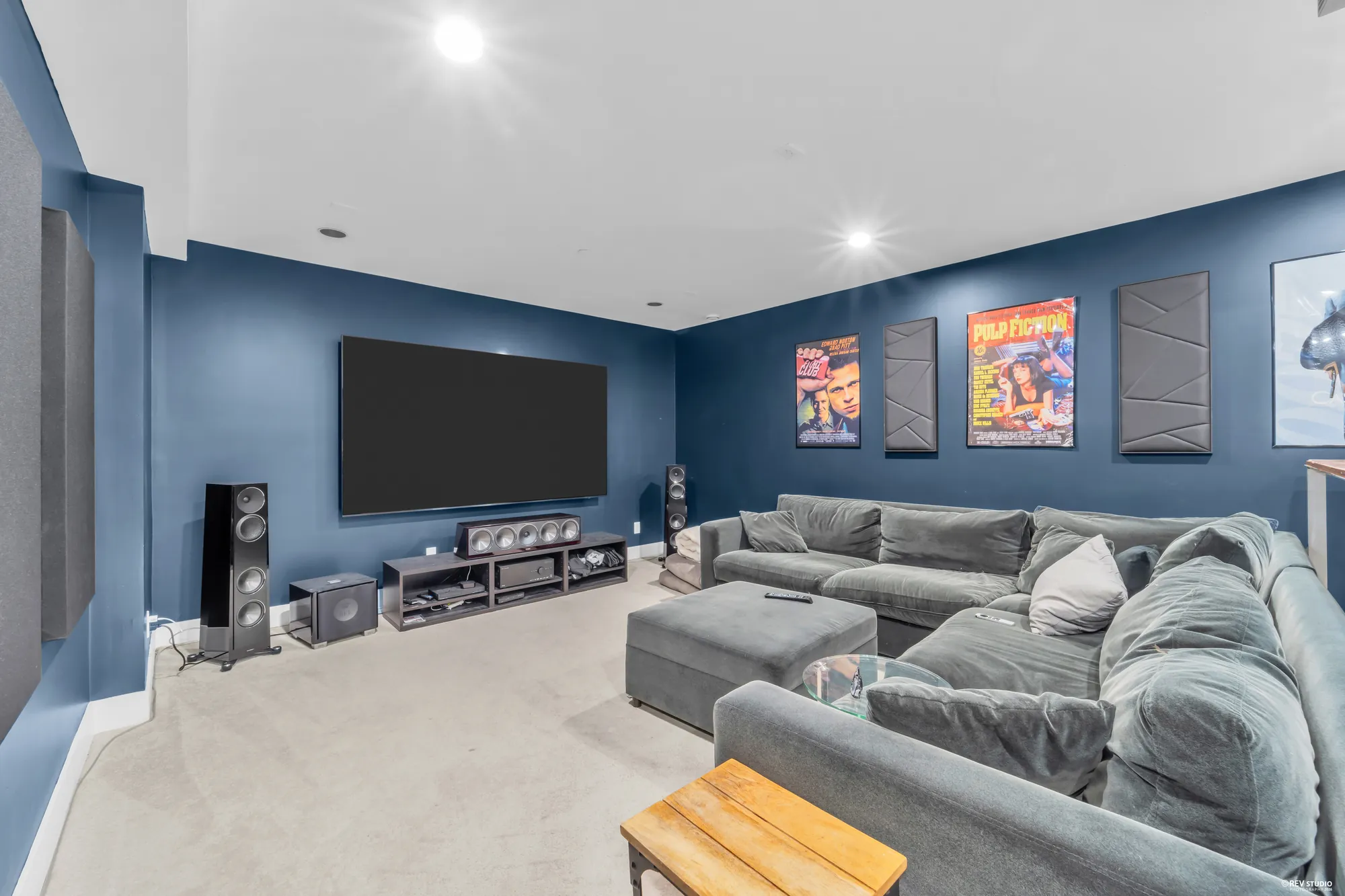 The theatre room: a large screen on the navy wall, acoustic panels, a grey sectional, film posters